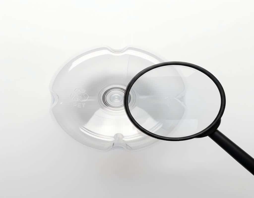 A Magnifying Glass Hovering Over The Base Of A Bottle, Enlarging The Recycling Symbol And Cavity Number To Show Their Detail.