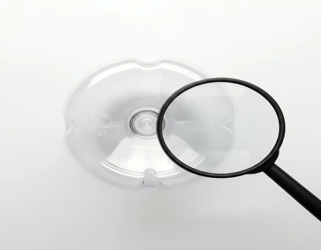 A Magnifying Glass Hovering Over The Base Of A Bottle, Enlarging The Recycling Symbol And Cavity Number To Show Their Detail.