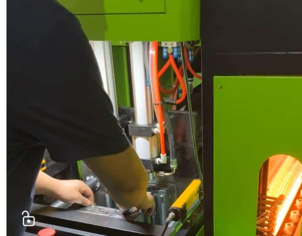 An Operator'S Hands Safely Placing A Hot Preform Into The Open Mold Of A Semi-Automatic Machine.