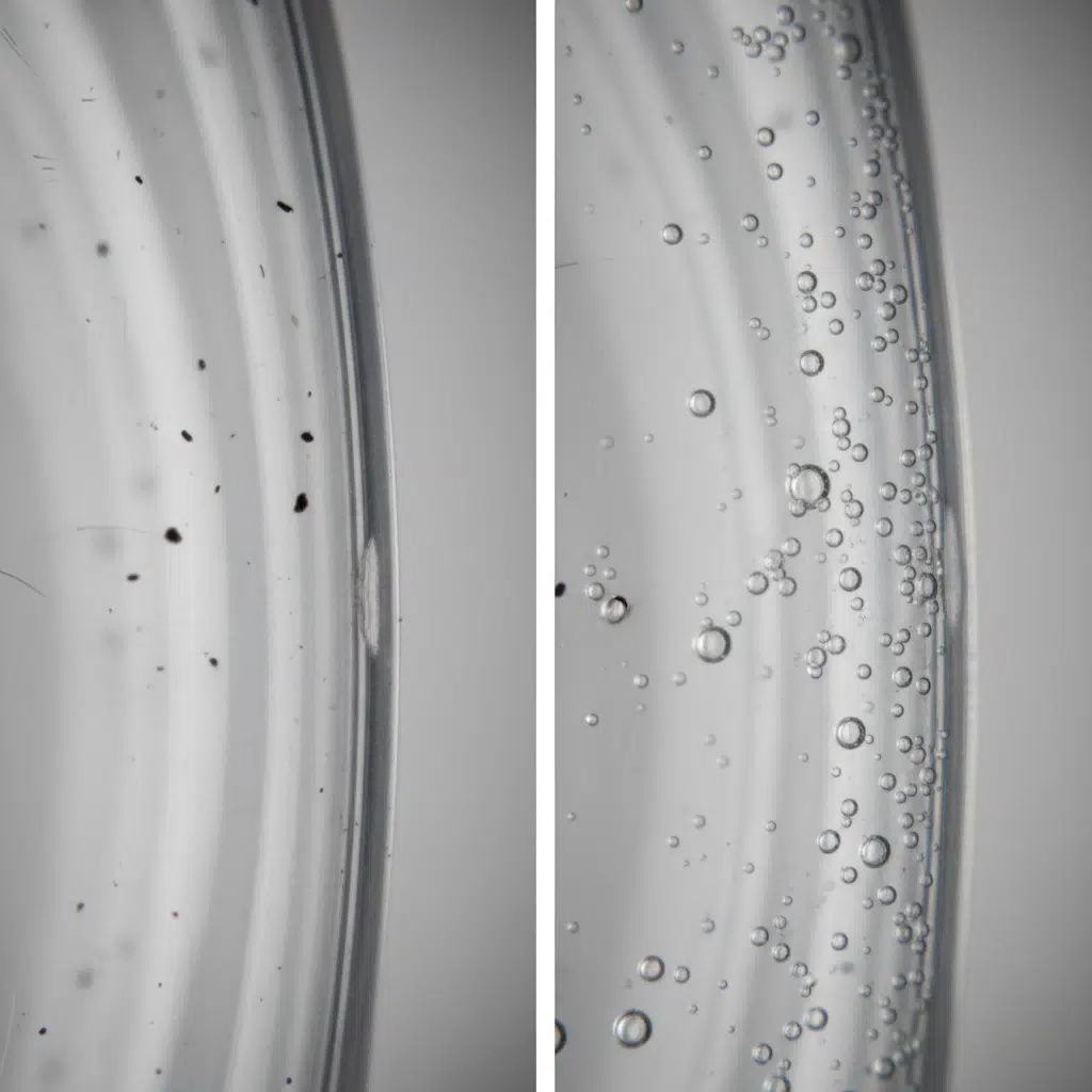 A Close-Up Of A Clear Pet Bottle Wall Showing Embedded Black Specks, And Another Bottle With Visible Air Bubbles In The Plastic.